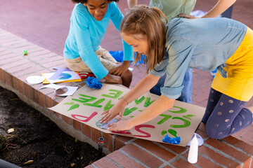 Happy diverse schoolchildren making ecology posters during outdoor school art class