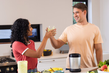 Making smoothies, young couple toasting with glasses in modern kitchen