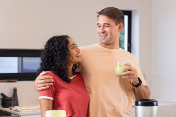 Smiling couple in kitchen enjoying healthy smoothies together, embracing each other - Powered by Adobe