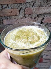 the hand holding a glass of smoothie that contain any vegetables with brick wall background.