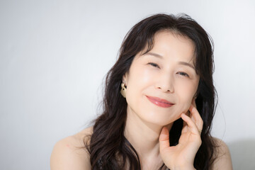 Fototapeta premium 頬に手を触れる女性のカメラ目線 美容やビューティーなどに 40代や50代の美しいスキンケアなどの健康的なイメージに