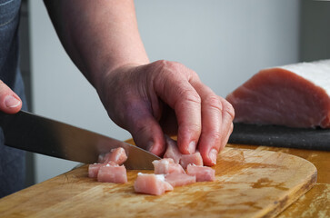 Hands of a seigners woman cutting a raw pork meat fillet on a wooden board with a knife
