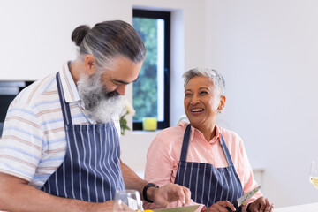 Senior couple wearing aprons cooking together and smiling in kitchen