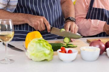 Chopping cucumber, senior couple preparing fresh salad in kitchen together