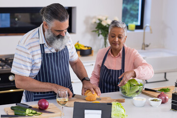 Chopping vegetables and using tablet, senior couple preparing meal together in kitchen