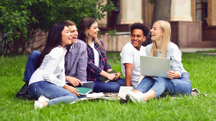 College students having discussion in campus, sitting on grass, preparing for exams