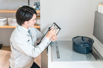 Obraz premium キッチンのIHコンロをチェックする設備会社・リフォーム業者・工務店の作業服姿の男性ビジネスマン 