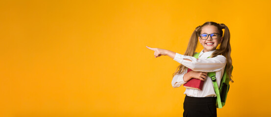 Look There. Cute Schoolgirl Pointing Finger At Copyspace Over Yellow Studio Background. Panorama © Prostock-studio