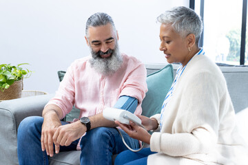 Obraz premium Checking blood pressure, woman using monitor on man sitting on couch