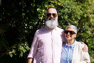 Senior couple wearing sunglasses, smiling and embracing outdoors in sunlight