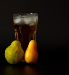 Pear juice from fruits of different varieties in a tall glass with ice on a black background, next to ripe fruits.