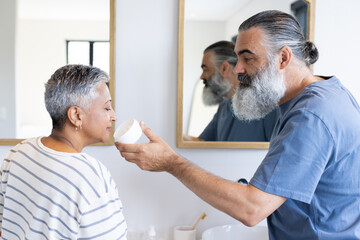 Applying face cream, senior man helping woman in bathroom, morning routine