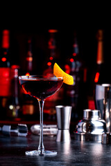Red cocktail drink with sherry, vermouth and orange zest, black bar counter background