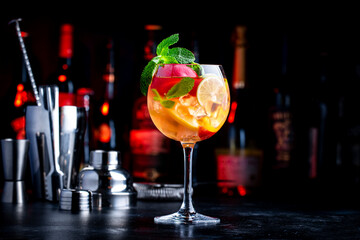 Summer sangria cocktail with pink wine, peach, orange and ice. Black background with  bottles