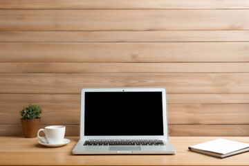Fototapeta premium Workplace with laptop having blank screen on wooden table with cup of coffee and notebook in front of wooden wall