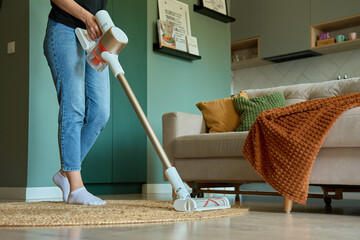 Woman is vacuuming floor of modern apartment living room, using portable cordless vacuum cleaner. Daily routine and household chores © Lazy_Bear