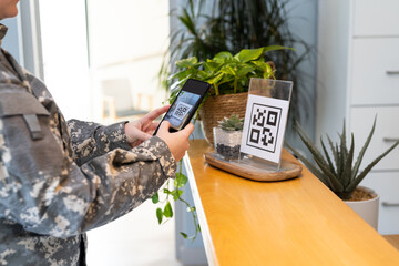 Scanning QR code with smartphone, person in undefined uniform at reception desk