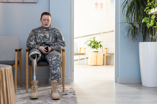 In waiting room, woman in undefined uniform with prosthetic leg using smartphone, copy space