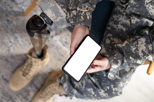 Holding smartphone, person in undefined uniform with prosthetic leg sitting indoors, copy space