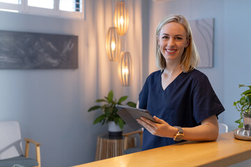 Smiling woman in medical clinic holding tablet, standing at reception desk, copy space