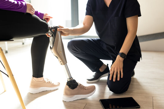 Adjusting prosthetic leg, healthcare professional assisting patient in clinic room