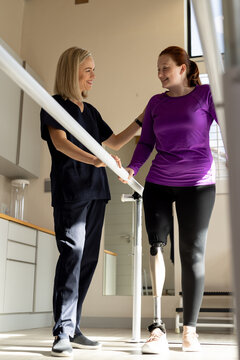 Woman in prosthetic leg walking with therapist on parallel bars in clinic