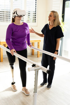 Woman in prosthetic leg walking using VR headset with therapist on parallel bars