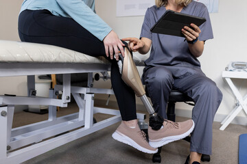 Patient with prosthetic leg consulting with therapist using tablet in clinic
