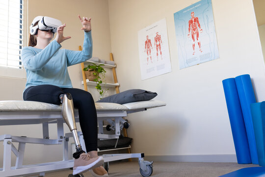 Using VR headset, woman with prosthetic leg sitting on medical examination table, copy space - Powered by Adobe