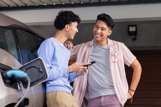 Charging electric car, two men smiling and talking in garage at home
