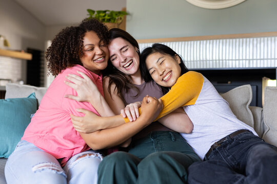Three women friends sitting on couch, hugging and smiling, enjoying time together