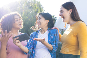 Smiling friends outdoors, holding smartphone and sharing exciting news together