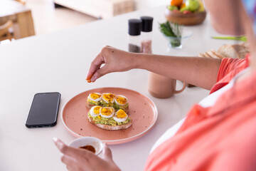 Preparing avocado toast with boiled eggs, woman seasoning food in kitchen