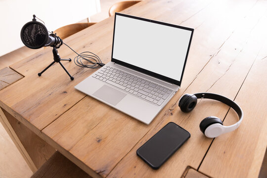 Podcasting setup with laptop, microphone, smartphone, and headphones on wooden table, copy space