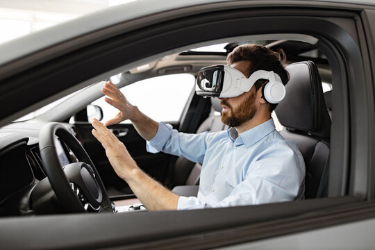Businessman uses virtual reality headset while sitting inside vehicle at dealership. Concept of innovative technology in automotive industry virtual test drives and immersive experiences for customers
