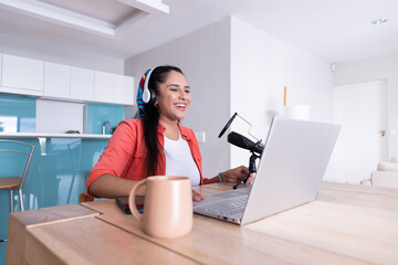 Recording podcast, woman using laptop and microphone in modern kitchen
