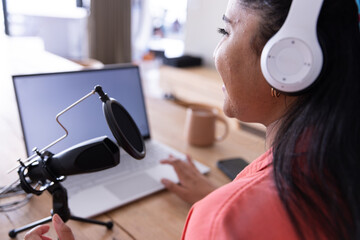 Recording podcast, woman using laptop and microphone with headphones in home office