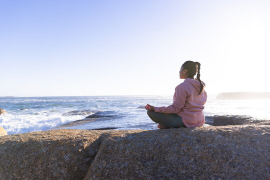 Meditating on rock by ocean, woman practicing mindfulness and relaxation techniques, copy space