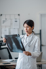 Female doctor in white coat examining an X-ray in a modern medical office, showcasing professional...