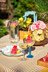 A bright summer garden setting in a yellow palette, with a yellow tablecloth, a vase of lemons with garden roses and watermelons