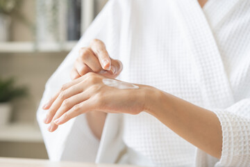 Health care, beauty asian young woman in bathrobe, towel after shower bath, spa relax at home, finger applying moisturizer on her back hand. Skin body cream moisturizing lotion, routine in morning.