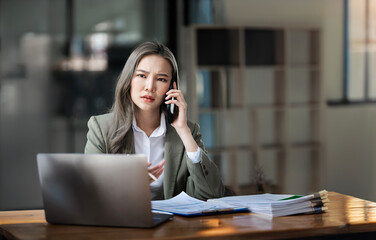 Serious female entrepreneur solving work's problem talking on telephone with colleague during distance job at modern computer.