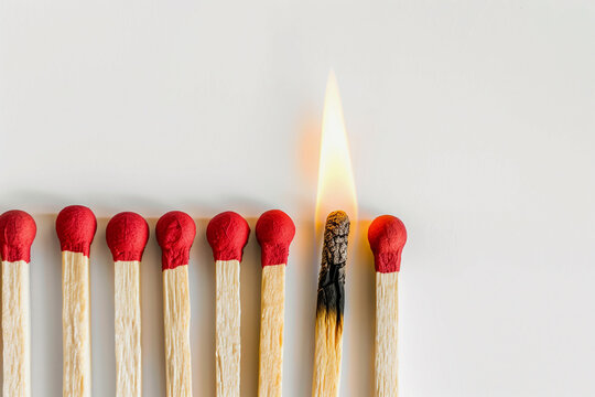 row of red and white matches with one of them having a single flame. Concept of a single spark or idea that can ignite a larger flame or movement