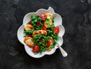 Halloumi cheese, cherry tomatoes, arugula salad - a delicious snack, appetizer on a dark background, top view