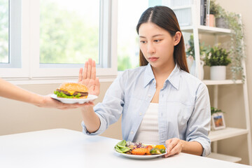 Diet concept, asian young woman hand reject eat burger, hamburger on plate, push out or deny to eat fast, junk food choose green vegetable salad, girl eat low fat for good healthy, getting weight loss