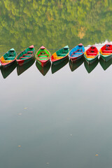 Fototapeta premium Colourful wooden boats on Phewa Lake in Pokhara, with space. Vertical photo.