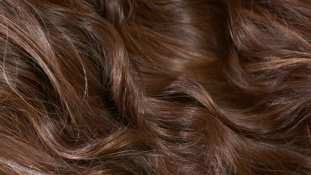 Close-up brown curly hair texture, female long hair background in slow motion