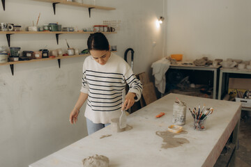 Serious creative female artisan standing at pottery workshop and making clay mug. Portrait of a focused artistic craftswoman standing at ceramics studio and making earthenware.Artisan making clay mug.