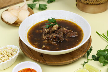 Rawon Daging Sapi or Indonesian beef black soup, traditional beef soup from East  Java, served with rice, bean sprouts, sambal, lime, and shrimp crackers.  