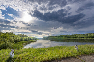A picturesque view of a calm lake surrounded by lush green trees and a bright blue sky with fluffy white clouds, hinting at a beautiful summer day in the Canadian wilderness.